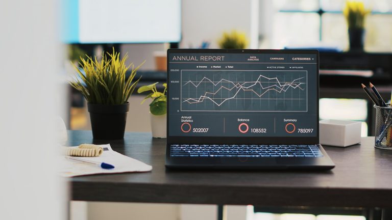 Laptop showing a campaign performance dashboard with multiple trend lines on an unattended office desk