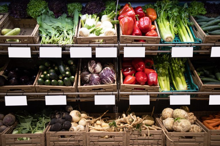 Rows of grocery produce crates with empty white shelf-edge label holders above each one