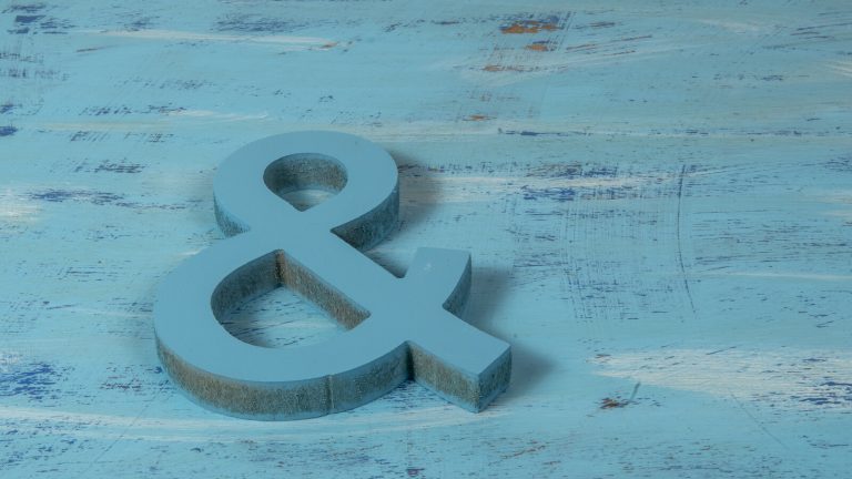 A solid blue ampersand sign lying on a weathered turquoise wooden surface